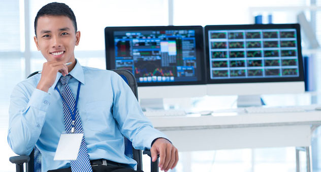 Satisfied analyst in shirt and tie sitting in front of two screens showing data and graphs