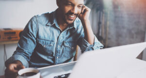 A man sitting at his laptop on a call, holding a cup of coffee.