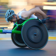 athlete in racing wheelchair moving at speed with background blurred