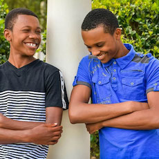 Two smiling young people lean against pillar in sunny garden