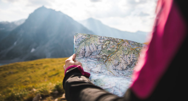 A woman sitting with a map in her hands. In the background is a mountainscape.