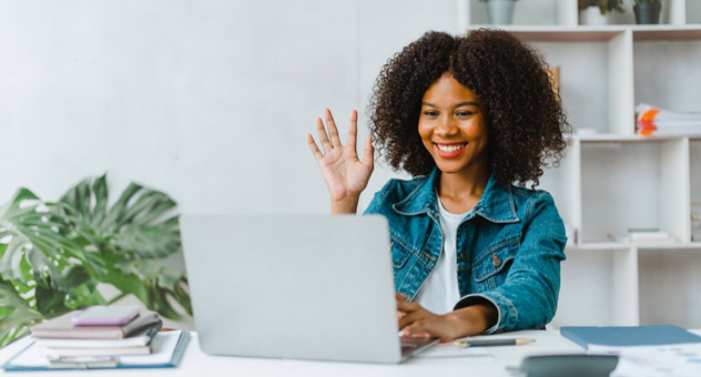 A woman smiling and waving to her laptop screen.