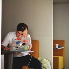 Young person with head in hand looking at laptop and sitting in cafe booth